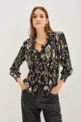Camisa de manga larga con cuello camisero y cierre frontal de botones. Presenta un estampado étnico tipo ikat en tonos negro, blanco y ocre.