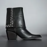 Botas estilo texanas color negro, con diseño de caña media que presenta un detalle de solapa decorada con tachas metálicas plateadas. Poseen taco cuadrado y punta fina.