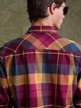 Camisa de manga larga en color azul noche con un patrón de cuadros finos en tonos rojos y verdes. Presenta cuello clásico, cierre frontal con botones y un bolsillo en el pecho con solapa.