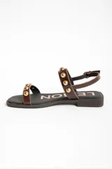 Sandalias planas de cuero marrón con tiras decoradas con tachas semiesféricas doradas, talón cerrado con tira ajustable y hebilla metálica.