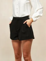Short de gamuza sintética color negro, de corte sastrero con pinzas frontales, bolsillos laterales y cierre con botón oculto.