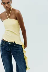 Top negro de cuello halter con lazada, escote recto y hombros descubiertos. Presenta un volante asimétrico en el lateral.