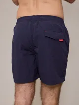 Short de baño azul marino con cintura elástica ajustable con cordón y logo de la marca bordado en rojo en la pierna izquierda.