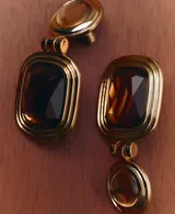 Aros colgantes dorados con diseño articulado, compuestos por una pieza circular superior con piedra semiesférica y una pieza rectangular inferior con piedra facetada color ámbar.