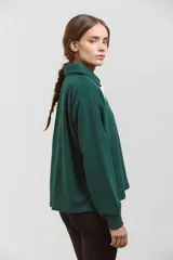 Buzo de algodón en color verde inglés, con diseño de cuello tipo chomba con botones frontales y detalles en blanco. Presenta un corte holgado y cómodo con mangas largas.