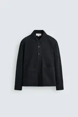 Camisa polo de denim negro con mezcla de algodón y cáñamo. Cuello polo con cierre frontal de tres botones. Manga larga con puño abotonado. Bolsillos de plastrón en el pecho y en la cadera.