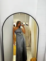 Vestido largo de fiesta confeccionado en tafeta con brillo, de corte ajustado al cuerpo con escote asimétrico de un solo hombro. Presenta una capa larga de seda liviana integrada que permite diversas formas de uso, aportando movimiento y elegancia.