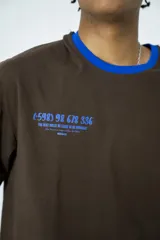 Remera oversize marrón con cuello y mangas con ribete azul. Estampado en la espalda con diseño de alfajores y texto en azul.