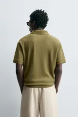 Polo de manga corta color verde oliva, con cuello solapa y abertura frontal tipo polo. Presenta una textura acanalada vertical y un calce regular.
