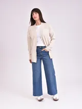 Cardigan abierto de punto color beige con bolsillos frontales y detalles de tejido acanalado en los hombros.