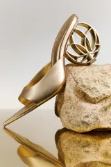 Sandalia tipo mule color dorado, con punta fina y un distintivo tacón escultórico de diseño circular calado.