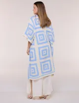 Cardigan largo confeccionado en tejido de punto calado estilo crochet, de color amarillo y blanco, con diseño geométrico de cuadrados, mangas amplias tipo kimono y corte abierto al frente.