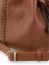 Cartera tipo morral de cuero graneado color marrón terracota, con formato de saco fruncido mediante tiras ajustables oscuras. Presenta una costura decorativa central con tientos a contratono y correa regulable.