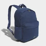Mochila Adidas de estilo clásico confeccionada en tejido de sarga de algodón color azul denim. Cuenta con un compartimento principal amplio, bolsillo frontal con cierre, bolsillos laterales elásticos y correas ajustables acolchadas con detalle de rayas. Presenta el logotipo del trébol de la marca en la parte inferior frontal.