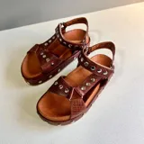 Sandalias de cuero marrón con textura croco, suela plataforma y tiras cruzadas decoradas con tachas metálicas plateadas. Cuentan con tira trasera ajustable con hebilla.