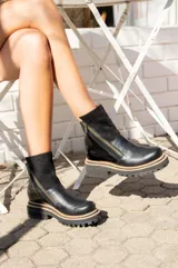 Botas cortas de cuero negro con paneles laterales de gamuza negra, cierre lateral con cremallera dorada y suela track con detalle de costura en color natural.