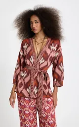 Kimono de punto Le Lis Blanc modelo Bina, con patrón jacquard geométrico en tonos rosados, marrones y crudo. Presenta escote en V profundo con ribete acanalado, mangas anchas de largo medio, corte holgado y cinturón de la misma tela para atar en la cintura.