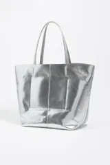 Bolso shopper de tamaño grande confeccionado en cuero reciclado con acabado metalizado plateado. Presenta doble asa superior, costura central vertical y logo de la marca bordado en el frente. Incluye cierre de mosquetón y bolsillo interior.