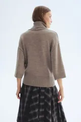 Buzo de punto fino suave color marrón, con mangas tres cuartos, cuello alto acanalado, hombros caídos y remates acanalados en puños y bajo.