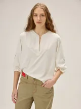 Remera de algodón de color off-white, con escote en V y mangas 3/4 abullonadas con puños elásticos fruncidos y detalles bordados.