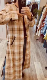 Tapado largo de paño liviano con diseño de cuadros en tonos marrones. Presenta solapas clásicas, bolsillos laterales con detalles en cuero y tajos profundos en los costados.