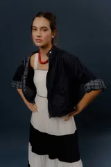 Campera de denim azul oscuro, de corte corto y estilo bomber, con cierre frontal y detalles de forrería a cuadros visibles en el interior de los puños.