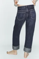 Pantalón de jean de tiro medio con corte recto y cinco bolsillos. Presenta un acabado con dobladillo ancho en el bajo y cierre frontal con botones metálicos.