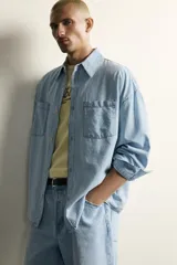 Camisa de corte relajado confeccionada en denim ligero de algodón, con cuello solapa, manga larga con puños abotonados y bolsillos de plastrón en el pecho. Presenta un acabado con efecto lavado y cierre frontal mediante botones.