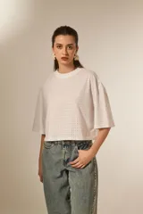 Remera blanca de corte holgado con mangas 3/4 y cuello redondo a la base. Presenta un diseño con apliques de studs metálicos distribuidos por toda la prenda.
