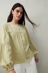 Camisa celeste de corte holgado con botones frontales, canesú con tablas y mangas 3/4 amplias con puño elastizado.