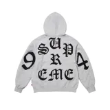 Hoodie gris de algodón con capucha, manga larga y bolsillo frontal tipo canguro. Presenta un diseño gráfico con letras negras en tipografía gótica que forman la palabra 'SUPREME' y el número '94' distribuidos en la espalda y mangas.