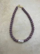 Collar artesanal compuesto por cuentas de piedra volcánica en diversos tonos y tamaños, con una perla natural de río como dije central y cierre metálico dorado.