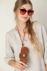 Estuche para lentes con correa larga para colgar al cuello, confeccionado en cuero color chocolate con cierre de broche metálico a presión.