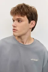 Remera de algodón gris con cuello redondo, corte oversize y pequeño logo bordado en contraste en el pecho con la inscripción "LE CLUB".