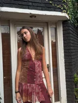 Vestido corto negro con escote en V profundo, estilo halter con tiras para atar al cuello. Presenta un diseño ajustado en el busto con tiras ajustables bajo el mismo que se cruzan y anudan en la espalda, y falda con volado en el ruedo con detalle de encaje.