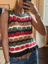 Top de punto sin mangas con diseño de rayas horizontales en negro, blanco, rojo, verde militar y marrón, intercaladas con círculos en relieve de los mismos colores. El dobladillo inferior es de punto con volantes.