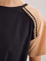 Remera de algodón con diseño bicolor, cuerpo en color negro y mangas en color beige. Presenta un detalle de galón trenzado en las costuras de las mangas raglán.