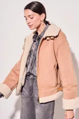 Campera gamulan color rosa con interior de piel sintética color crema, cierre frontal con cremallera y hebillas en el cuello. Corte oversize.