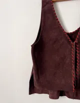 Chaleco marrón de cuero gamuzado con costuras rojas en los bordes y cierre con cordones en el frente.