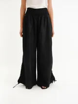 Pantalón negro de lino con cintura elástica fruncida y pernera ancha, con detalles de cordones ajustables a los lados.