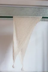 Chal triangular tejido a mano en lana de alpaca natural color crudo, con diseño calado y terminación con borlas.