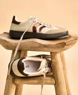 Zapatillas beige con detalles en gamuza, franjas laterales bordadas en animal print y bordó, y talón en cuero marrón oscuro. Tienen cordones beige y suela de plataforma negra.