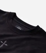 Remera oversize de tejido tipo gamuza sintética negra, con cuello redondo, manga corta y bordado de cruz gótica en el pecho.