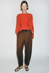 Pantalón tiro bajo color marrón, de corte globo y pernera recta con raya marcada al frente. Incluye trabillas y un cinturón marrón oscuro con hebilla metálica.