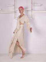 Conjunto de falda larga y top de algodón color crema. La falda tiene tajos laterales y lazo en la cintura. El top tiene escote regulable con nudo y mangas largas con detalle de puntilla en los puños.