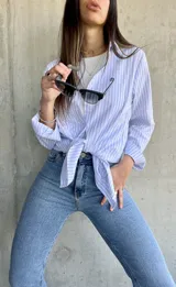 Camisa de manga larga con rayas verticales celestes y blancas, de corte recto y largo con aberturas laterales.