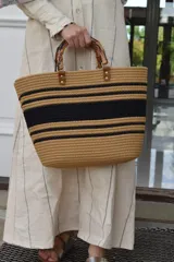 Bolso de hombro tipo tote a rayas marrones y negras, confeccionado en tejido texturizado con asas rígidas de bambú y detalles en cuerina marrón con tachas metálicas.