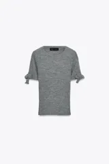 Jersey de punto acanalado en color gris, con cuello redondo y mangas cortas que presentan detalles de lazos ajustables en los extremos.