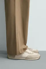 Zapatilla deportiva estilo barefoot, color marrón, con diseño de paneles en combinación de materiales y detalles en serraje. Cuenta con puntera redondeada y ancha, cordones en color crema y suela fina de goma flexible en contraste.