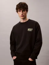 Buzo Calvin Klein de felpa color negro, con cuello redondo, manga larga, puños y dobladillo acanalados. Presenta un bordado frontal con la palabra "VERY" en tonos verdosos y debajo el logo de la marca.